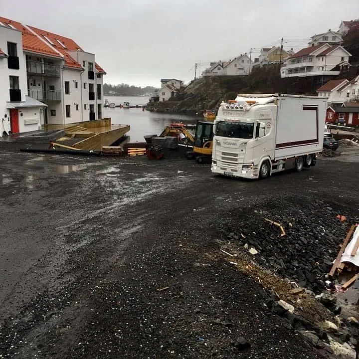 Scania-lastebil ved havnen med anleggsmaskiner og bygninger.