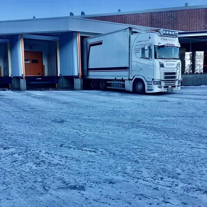 En hvit Scania-lastebil fra Utne Transport parkert ved en lasterampe på et isdekt underlag.